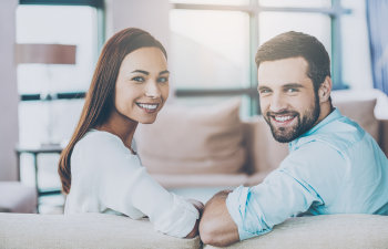 A happy young couple with a perfect smiles sitting on a sofa.