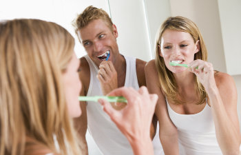A cheerful young couple brushing their teeth in front of a mirror.