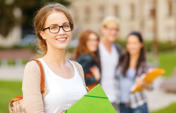 A broadly smiling student girl wearing glasses carrying folders.