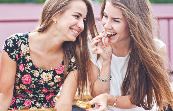 Two cheerful young women with perfect smiles having lunch outdoors.