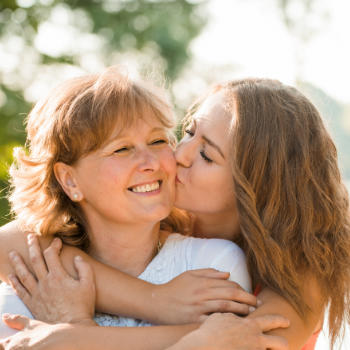 A young woman kissing oheek her happily smiling mother.