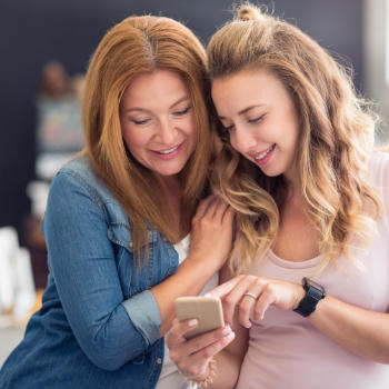 A teenage girl showing something on her phone to her mother.