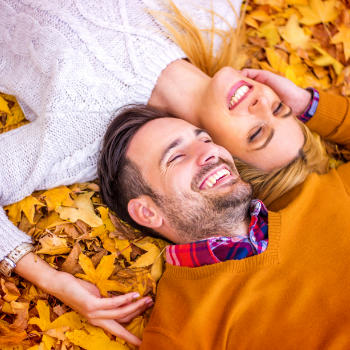 Happy mature couple with perfect smiles lying on autumn leaves in a park.
