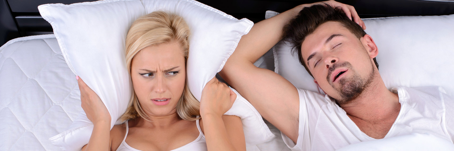 An annoyed woman covering her ears with a pillow due to her partner's snoring.