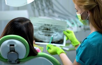 A dentist showing teeth x-rays and explaining treatment to a patient sitting in a dental chair.