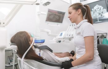 Dentist talking to her patient sitting with a sedation mask in a dental chair.